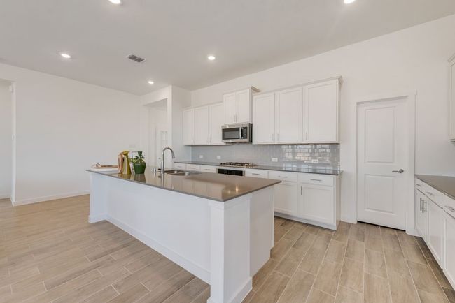 Kitchen with appliances with stainless steel finishes, light wood-style flooring, backsplash, a center island with sink, and white cabinetry | Image 10