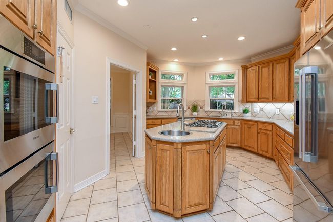 This spacious kitchen features beautiful wood cabinetry, a central island with a gas cooktop and sink, modern appliances, and ample natural light from multiple windows, creating an inviting space for cooking and entertaining. | Image 20