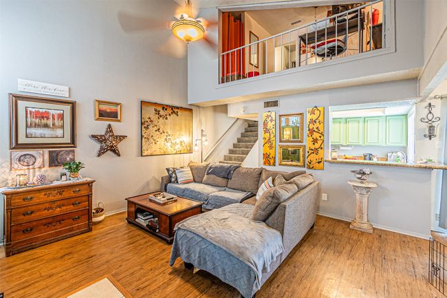Living room featuring a ceiling fan, a towering ceiling, wood finished floors, stairs, and baseboards | Image 6