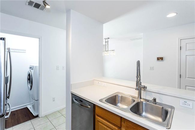 Kitchen featuring appliances with stainless steel finishes, brown cabinetry, light countertops, light tile patterned floors, and washer / dryer | Image 8