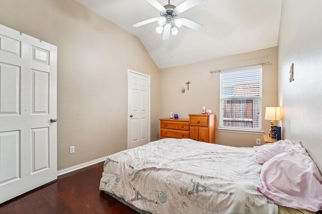 Cozy bedroom with vaulted ceiling, ceiling fan, and warm hardwood floors. Features a window for natural light, neutral walls, and ample storage with a closet and wooden dresser. | Image 22