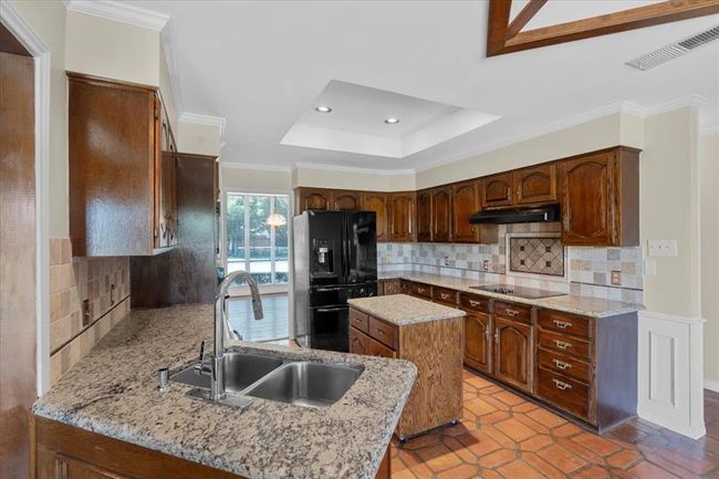 Kitchen featuring black appliances, light tile patterned floors, sink, kitchen peninsula, and backsplash | Image 7