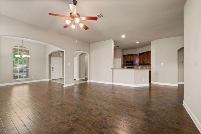 Unfurnished living room featuring ceiling fan with notable chandelier, arched walkways, dark wood-type flooring, visible vents, and recessed lighting | Image 7