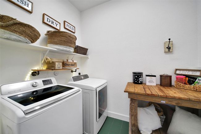 This laundry room features a modern washer and dryer set, open shelving with woven baskets for storage, and a rustic wooden folding table. The space is well-organized and has decorative touches for a cozy feel. | Image 39
