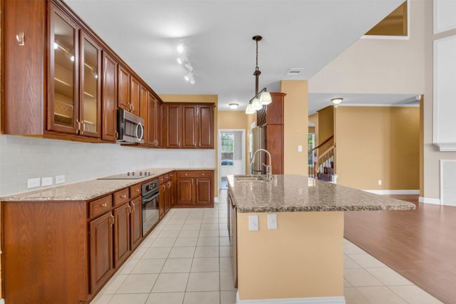Kitchen featuring stainless steel microwave, black oven, electric stovetop, light tile patterned floors, and glass insert cabinets | Image 8