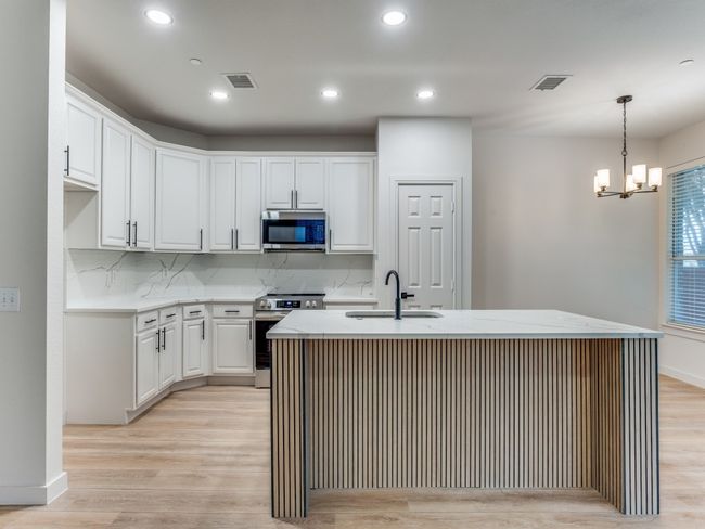Kitchen featuring stainless steel appliances, white cabinetry, light wood-style flooring, a chandelier, and recessed lighting | Image 12