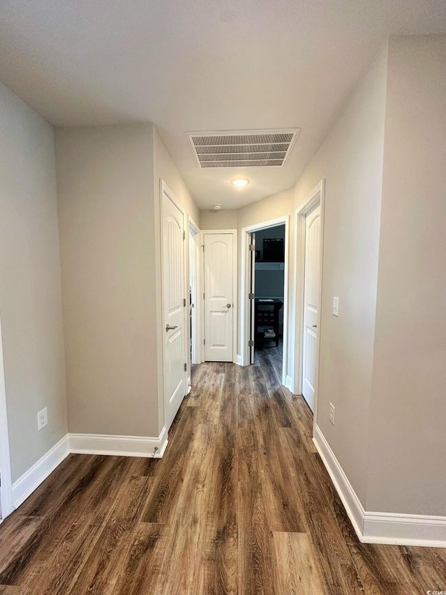 Corridor with dark wood-style flooring, baseboards, and visible vents | Image 4