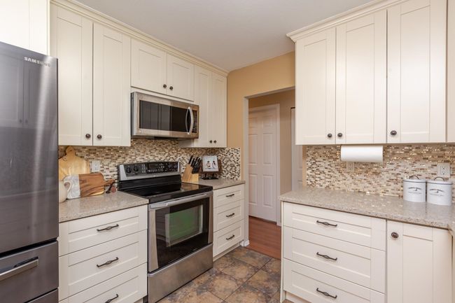 Kitchen with light stone counters, cream cabinets, stainless steel appliances, and decorative backsplash | Image 12