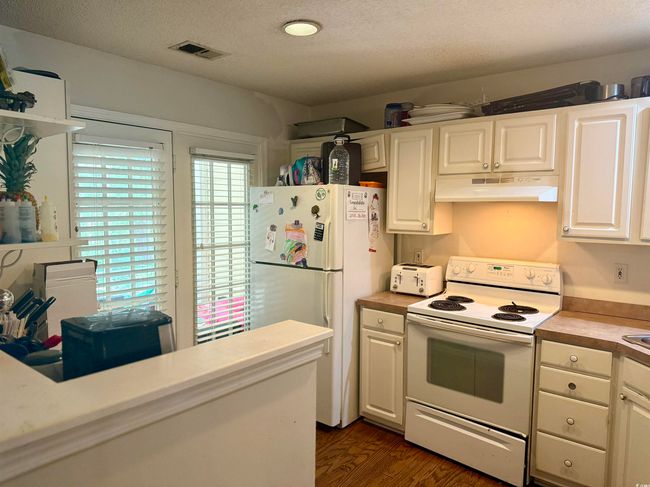 Kitchen with white appliances, under cabinet range hood, light countertops, white cabinetry, and a textured ceiling | Image 4