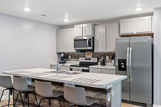 Kitchen with appliances with stainless steel finishes, a breakfast bar, and a center island with sink | Image 9
