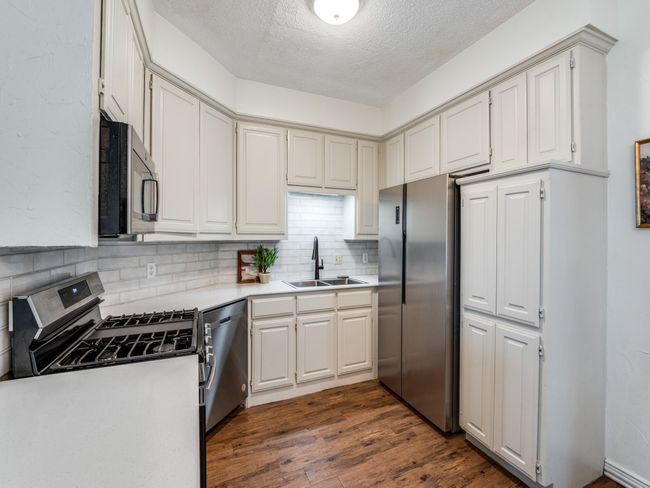 Kitchen with appliances with stainless steel finishes, backsplash, a textured ceiling, dark wood-type flooring, and light countertops | Image 10