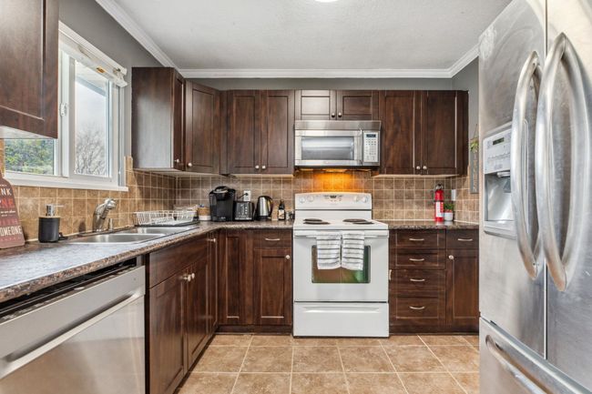 Kitchen featuring light tile patterned floors, a sink, crown molding, stainless steel appliances, and decorative backsplash | Image 14