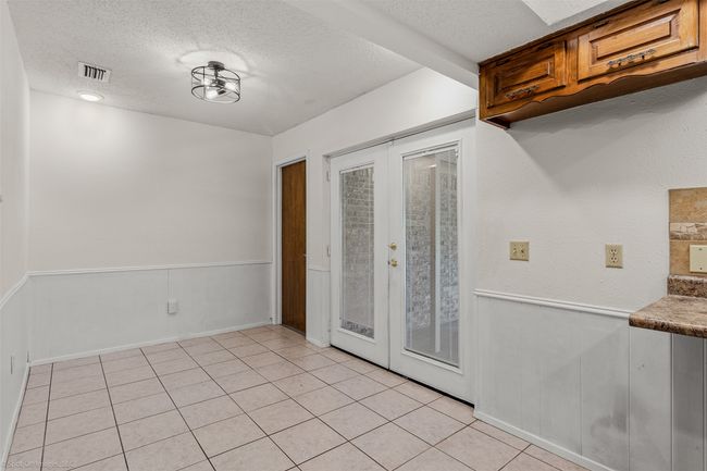 Unfurnished dining area with french doors, a textured ceiling, wainscoting, and light tile patterned flooring | Image 13