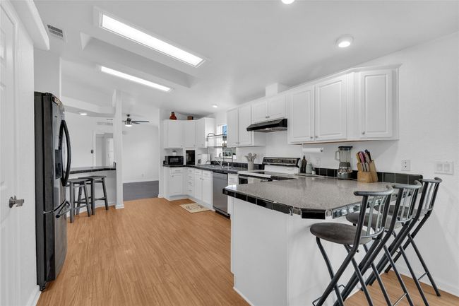 Kitchen with black fridge with ice dispenser, under cabinet range hood, a peninsula, electric range oven, and white cabinets | Image 11