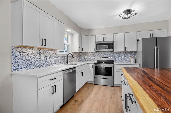 Kitchen featuring butcher block countertops, stainless steel appliances, white cabinets, and backsplash | Image 11