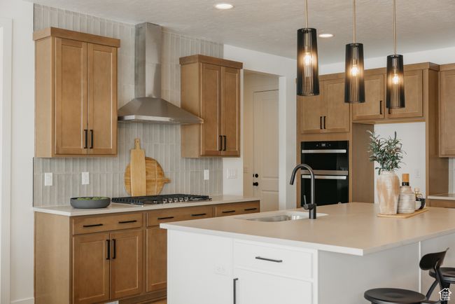 Kitchen with wall chimney exhaust hood, stainless steel gas cooktop, a sink, tasteful backsplash, and a center island with sink | Image 17
