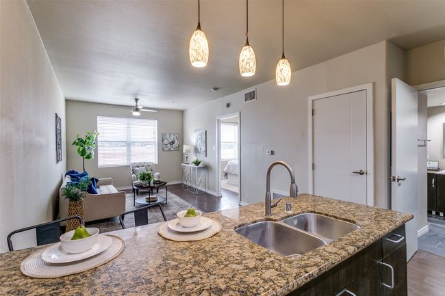 Kitchen featuring open floor plan, dark wood finished floors, a ceiling fan, pendant lighting, and light stone countertops | Image 8