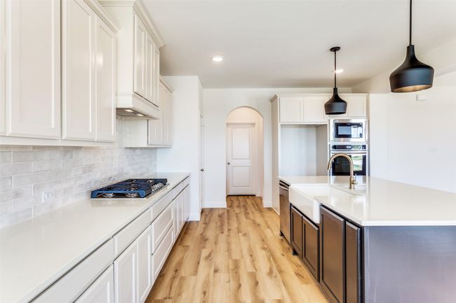 Kitchen with light hardwood / wood-style floors, tasteful backsplash, stainless steel appliances, hanging light fixtures, and white cabinets | Image 9