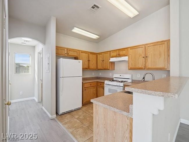 Kitchen with a peninsula, light countertops, white appliances, vaulted ceiling, and a kitchen bar | Image 6