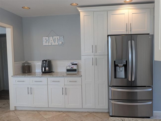 Kitchen with stainless steel refrigerator with ice dispenser, stone countertops, white cabinets, tasteful backsplash, and tile floors | Image 10