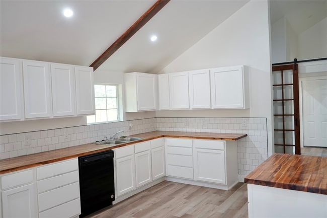 Kitchen featuring wooden counters, dishwasher, decorative backsplash, light wood-style floors, and white cabinetry | Image 7