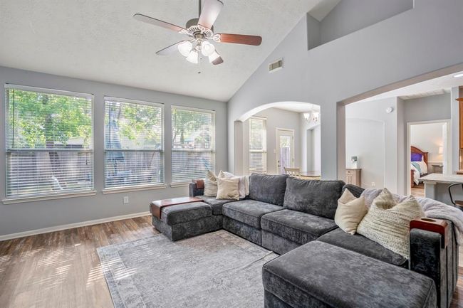 From near the fireplace, this view captures the backyard through large windows that fill the space with natural light. Just off the kitchen, a glimpse into the downstairs primary bedroom highlights the home’s thoughtful layout. | Image 9