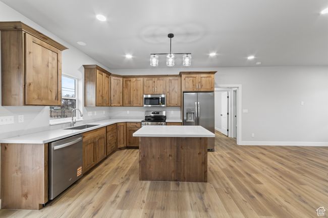 Kitchen featuring light countertops, light wood-style flooring, appliances with stainless steel finishes, a sink, and a center island | Image 13
