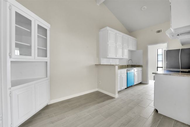 Kitchen featuring freestanding refrigerator, dishwashing machine, white cabinets, high vaulted ceiling, and light stone counters | Image 4