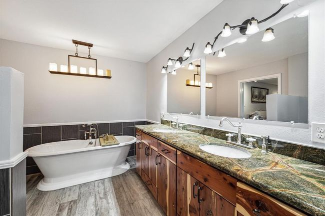 This beautiful primary bathroom has been remodeled with new tile flooring, custom cedar cabinetry, granite counter tops, and lighting. Enjoy the authentic cast iron soaking tub to relax after a long day | Image 8