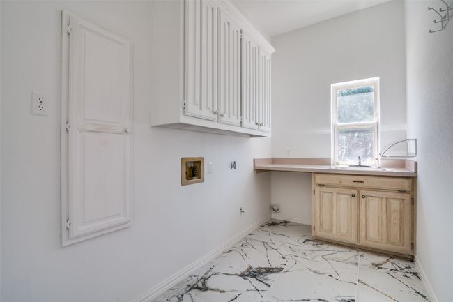 Laundry area with washer hookup, cabinet space, light marble finish flooring, and baseboards | Image 18