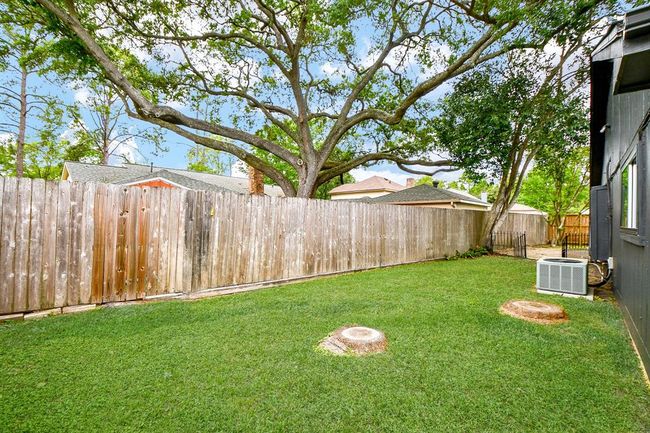 Spacious backyard with a well-maintained lawn, mature trees providing shade, and a wooden fence for privacy. Ideal for outdoor activities and entertaining. | Image 47