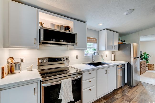 Kitchen featuring stainless steel appliances, a sink, wood finished floors, decorative backsplash, and light countertops | Image 11