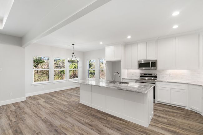 Kitchen with light stone countertops, stainless steel appliances, a kitchen island with sink, pendant lighting, and white cabinetry | Image 13