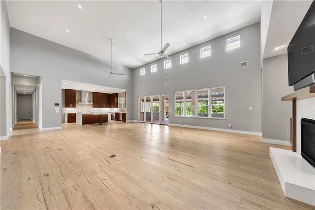 Unfurnished living room featuring a towering ceiling, a ceiling fan, a fireplace with raised hearth, and light wood-type flooring | Image 7