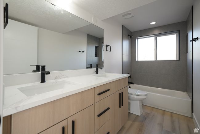 Bathroom featuring wood finished floors, toilet, double vanity, shower combination, and a textured ceiling | Image 28