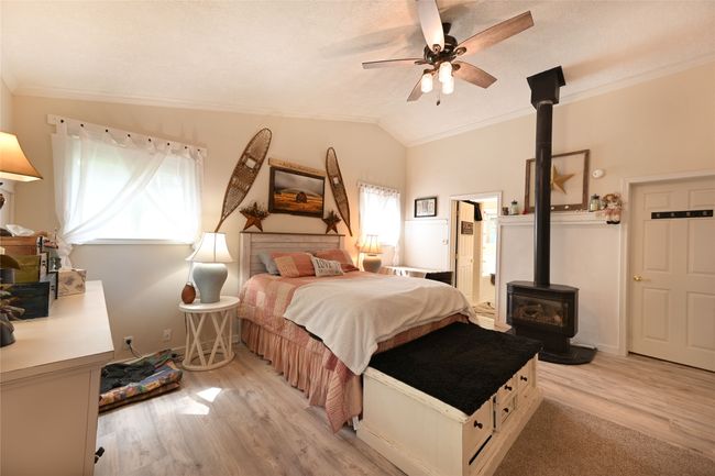 Bedroom featuring a wood stove, light wood finished floors, crown molding, lofted ceiling, and a ceiling fan | Image 32