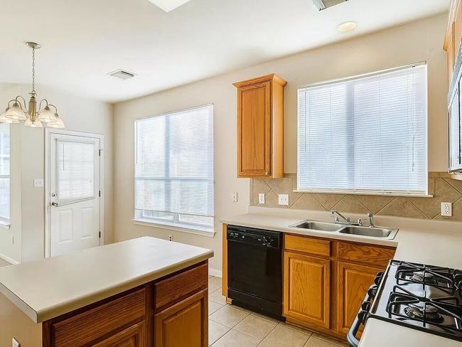 Kitchen with black dishwasher, a sink, gas stove, light tile patterned floors, and a chandelier | Image 11