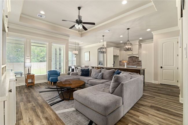 Welcome to the open family room that offers a spacious and inviting atmosphere with a raised ceiling, ceiling fan, wood-look vinyl flooring, elegant ornamental molding, and recessed lighting for a polished finish. | Image 6