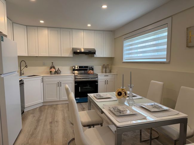 Kitchen with stainless steel appliances, ventilation hood, light wood finished floors, recessed lighting, and white cabinetry | Image 23