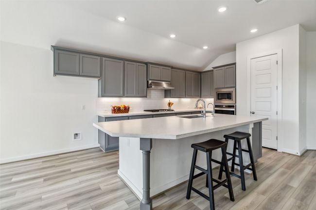 Kitchen with under cabinet range hood, stainless steel appliances, light countertops, light wood finished floors, and vaulted ceiling | Image 9