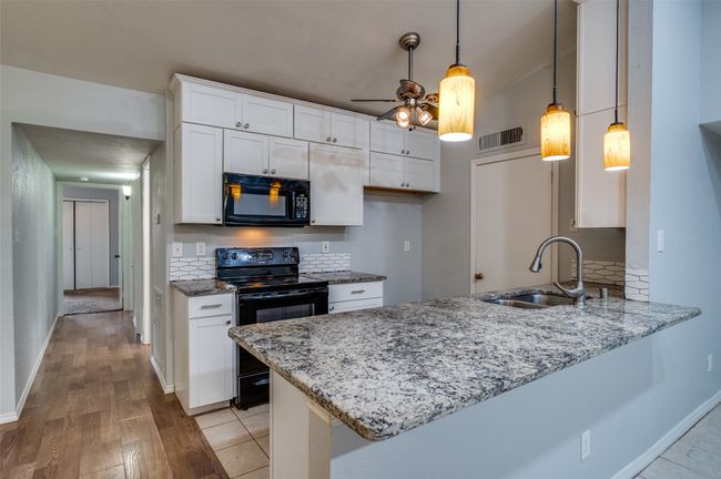 Kitchen featuring black appliances, a peninsula, light wood-style floors, light stone counters, and white cabinets | Image 4