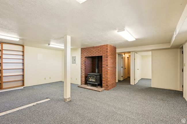Finished basement with a wood stove, carpet flooring, a textured ceiling, and electric panel | Image 28