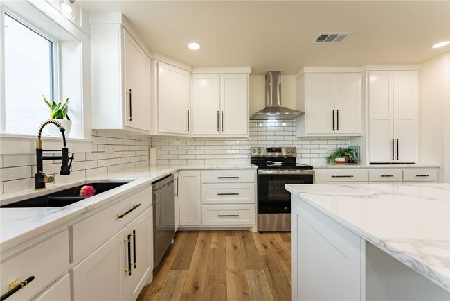 Kitchen featuring stainless steel appliances, a sink, visible vents, white cabinets, and wall chimney exhaust hood | Image 4