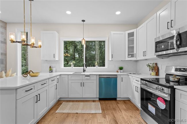 Kitchen with appliances with stainless steel finishes, light wood finished floors, a peninsula, a chandelier, and white cabinetry | Image 12