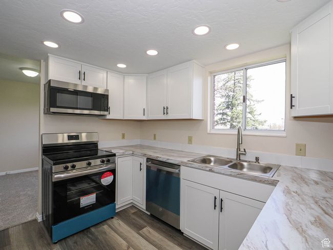 Kitchen featuring appliances with stainless steel finishes, white cabinets, dark wood-style flooring, recessed lighting, and light stone counters | Image 30
