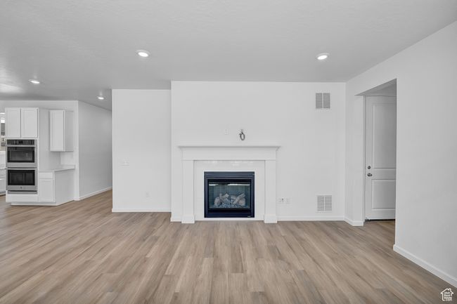 Unfurnished living room with light wood-style flooring, baseboards, a glass covered fireplace, and recessed lighting | Image 5