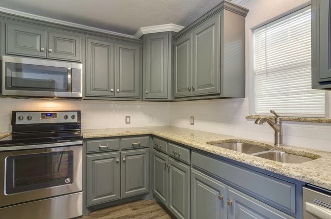 Kitchen with appliances with stainless steel finishes, gray cabinets, backsplash, dark wood-style floors, and light stone countertops | Image 14