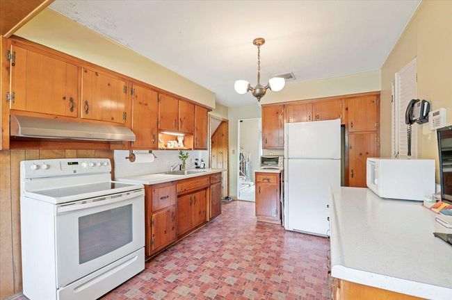 Kitchen with white appliances, under cabinet range hood, light countertops, and brown cabinetry | Image 11