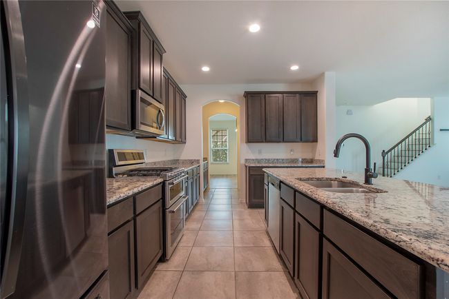 Kitchen featuring appliances with stainless steel finishes, arched walkways, dark brown cabinetry, light stone countertops, and recessed lighting | Image 14