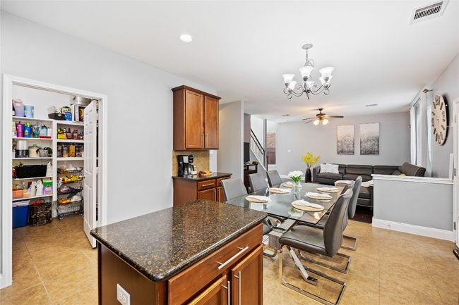 Kitchen with a chandelier, light tile patterned floors, brown cabinets, pendant lighting, and dark stone countertops | Image 11